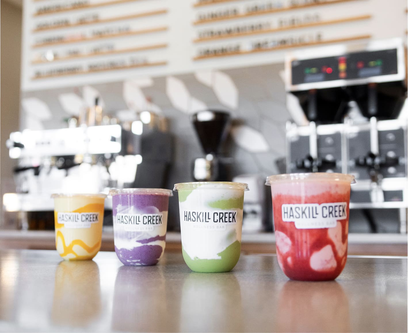 Haskill Creek Wellness Bar counter featuring a professional espresso machine and a row of colorful superfood smoothies in unique round cups.